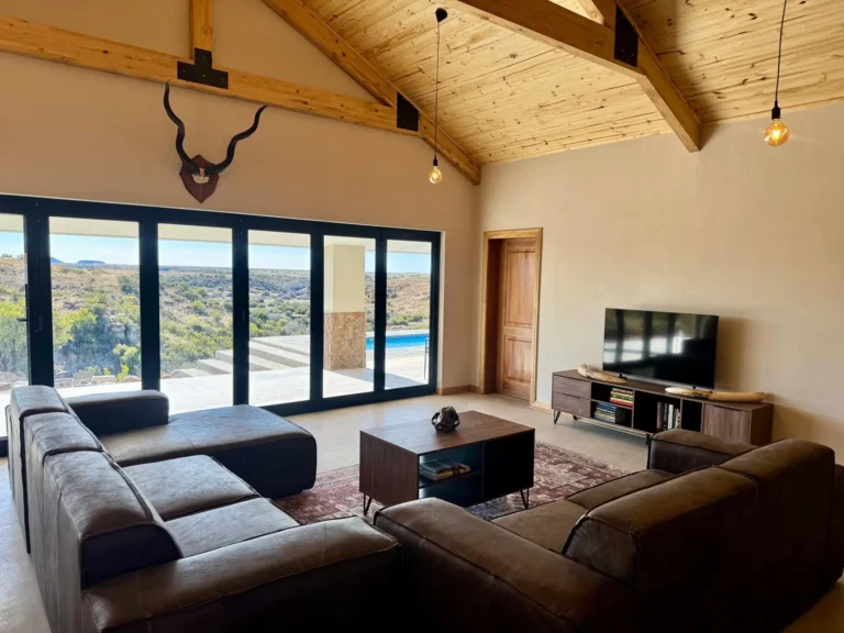 Wohnzimmer der Lodge mit Sofas und Panoramafenstern zum Busch
