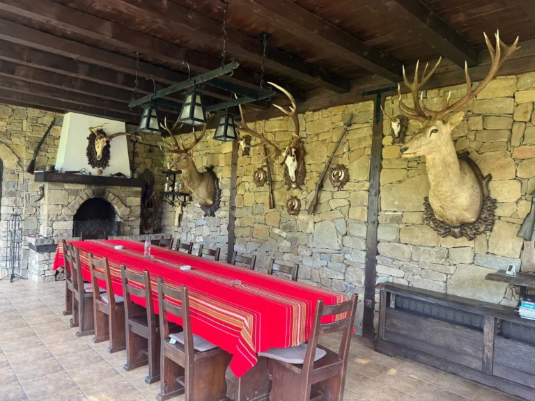 Speisebereich im Jagdhaus mit Natursteinwand, Kamin und Rothirsch-Trophäen über einer langen Tafel