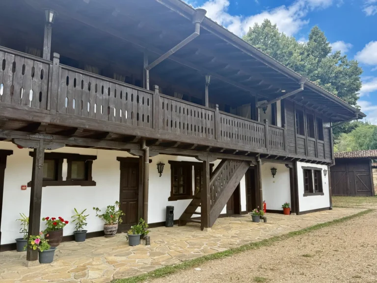 Traditionelles bulgarisches Jagdhaus mit Holzbalkon, weißen Wänden und Blumen im Innenhof