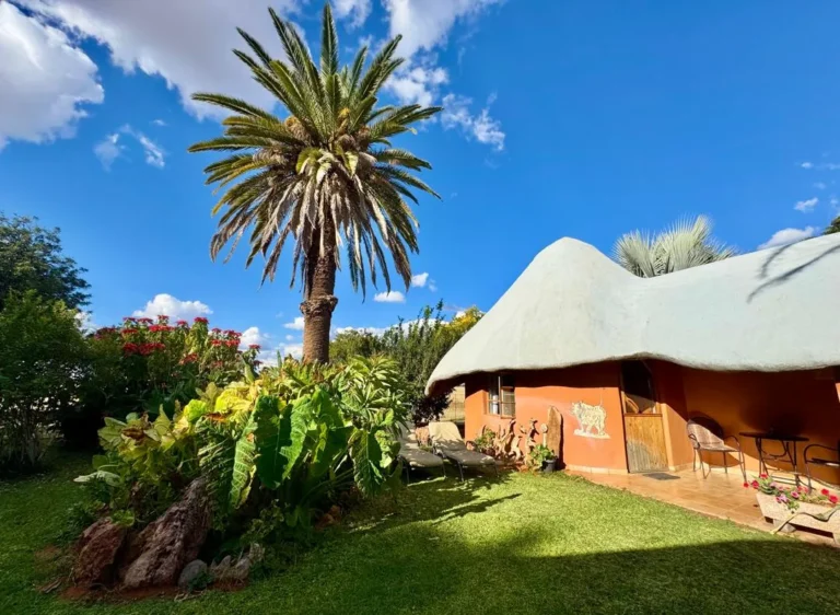 Gästehaus mit Strohdach und Palme im Garten der Jagdfarm in der Kalahari, Namibia